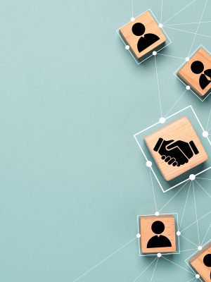 Top view design on blue background of Hand shaking which print screen on wooden cube block which connection with human icon for business deal and agreement concept.